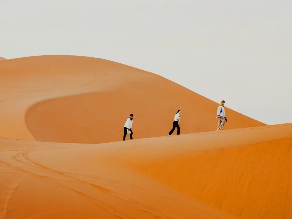 Trois voyageurs marchant sur la crête d'une dune orange du Sahara